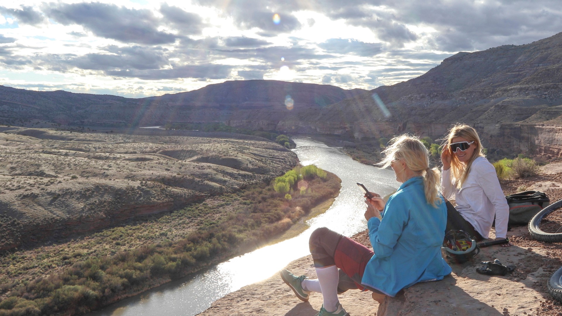 Mother and daughter mountain bikers relax on canyon ridge above river